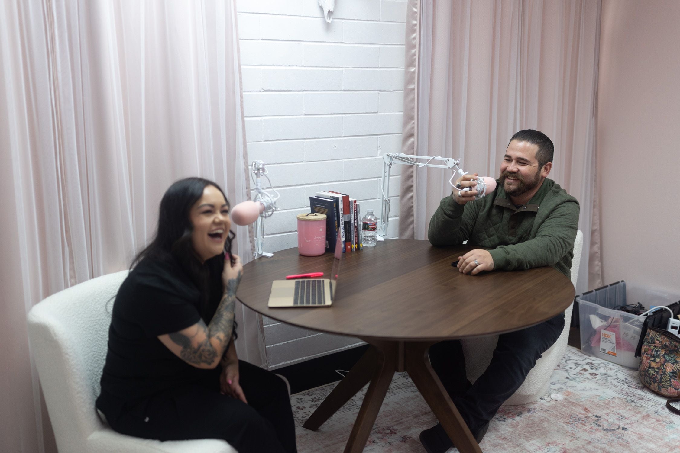 Photo of Bree, owner of Rebel Wax and a man laughing while sitting at a table speaking into microphones.