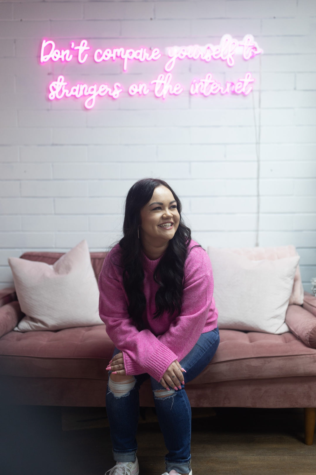 Photo of Lash and Wax OC owner Bree smiling while sitting on a pink couch.