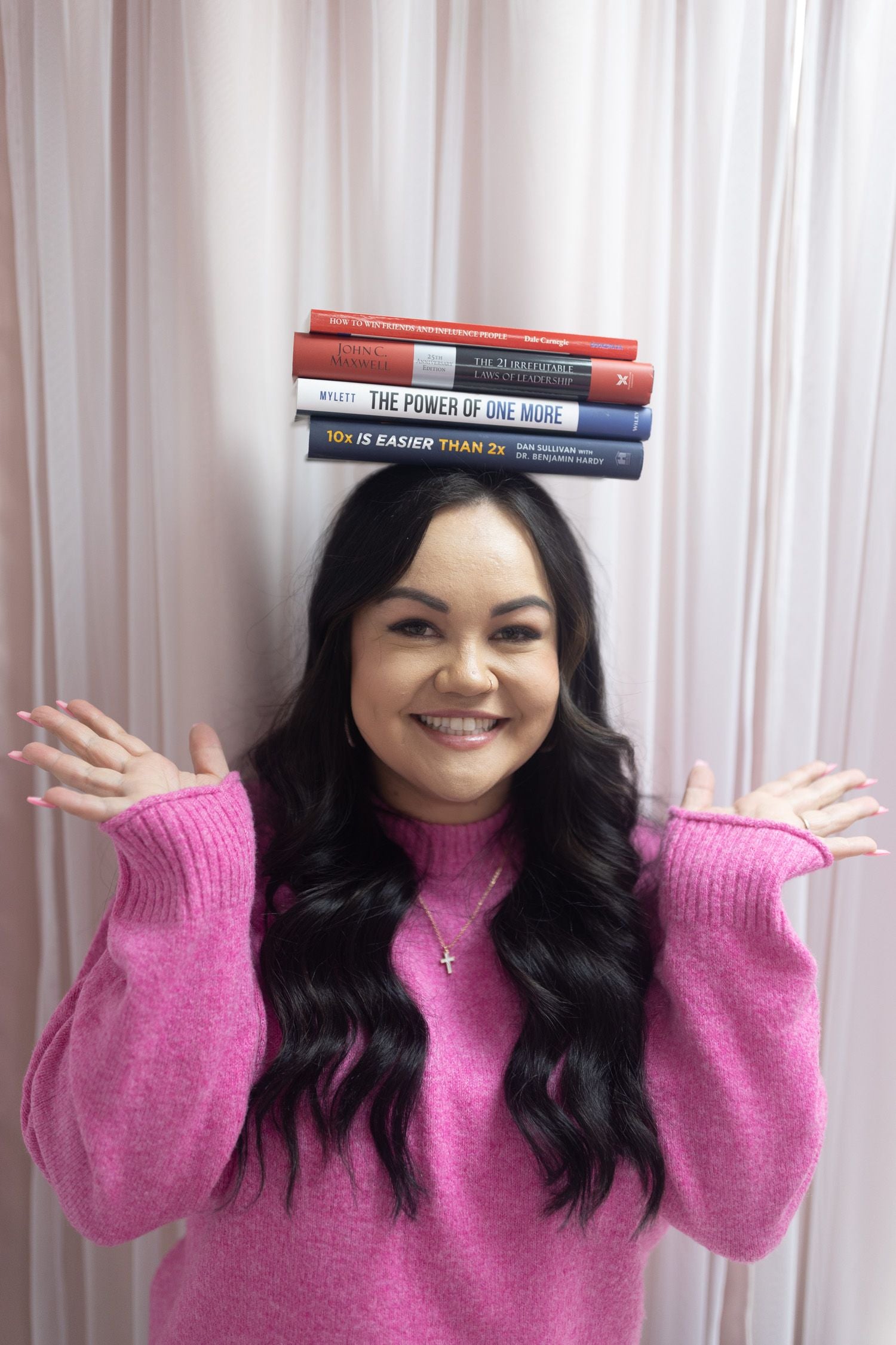 Photo of Lash and Wax OC owner Bree smiling while balancing a stack of books on her head.